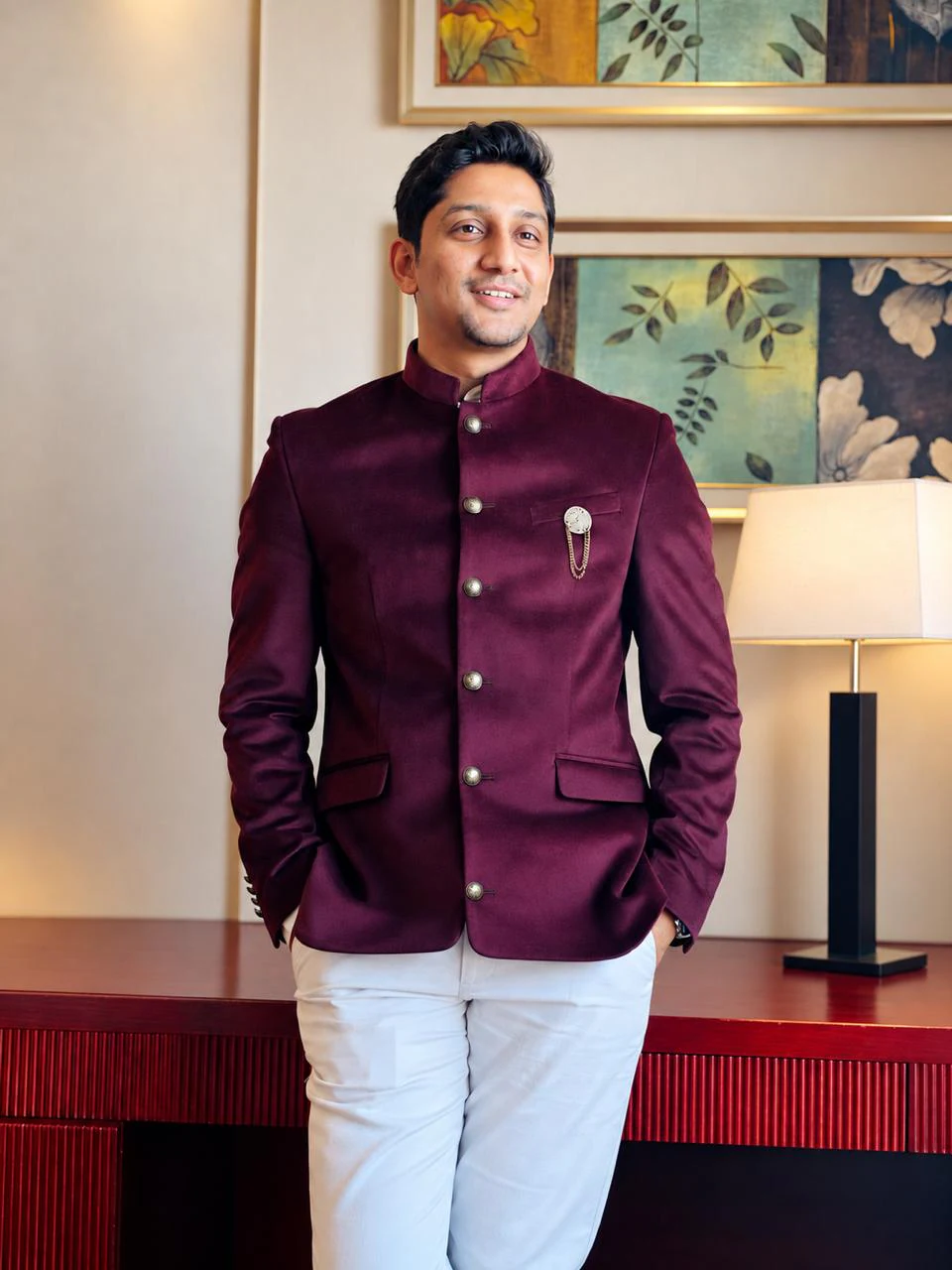 Gaurav Singh Bisht in a maroon bandhgala jacket, smiling, standing at a red wooden console